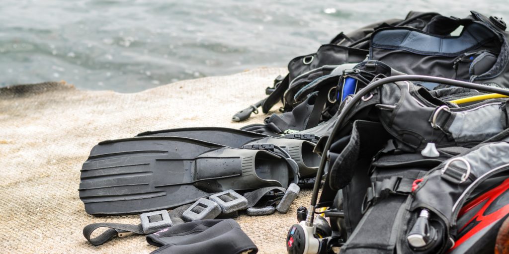 Pile of Scuba Diving Equipment Including Fins and Weights Drying on Coastal Dock near Water