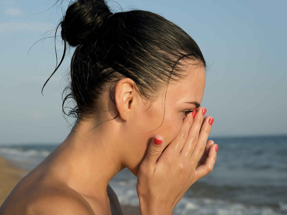 Close-up of a young woman rubbing irritated sensitive eyes on the beach, allergy reaction